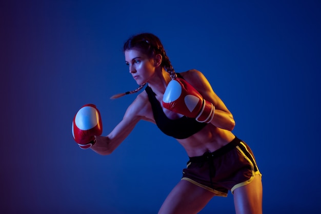 Fit donna caucasica nella boxe di abbigliamento sportivo su sfondo blu studio in luce al neon
