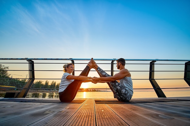 Fit giovane coppia che fa acro yoga al molo in riva al mare stile di vita sano persone attività sportiva all'aperto ...