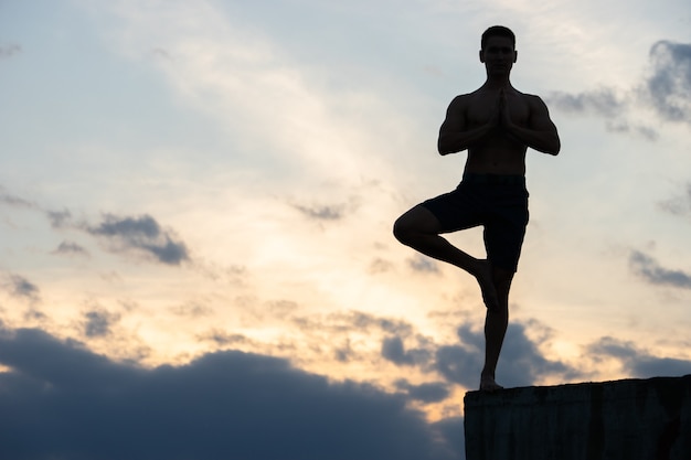 Fit giovane uomo pratica yoga saluto al sole sul bordo della scogliera al tramonto.