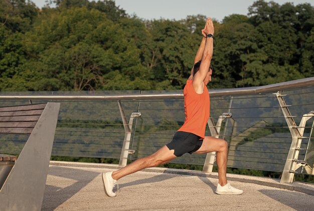 Fit man tenere virabhadrasana posa facendo allungamento affondo a mezzaluna sul lungomare di yoga