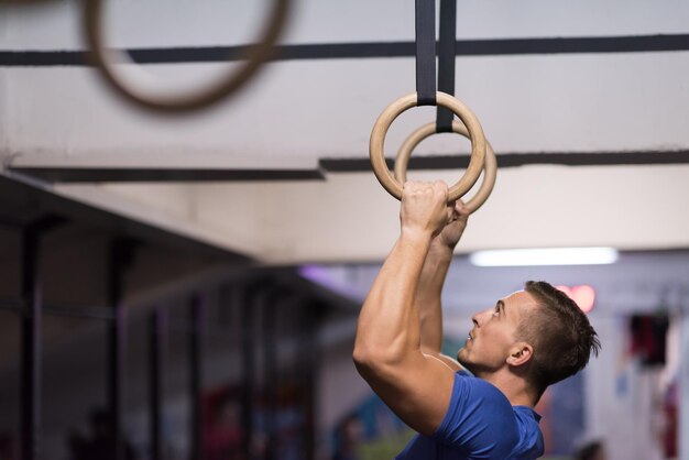 Fitness bell'uomo che fa esercizio di immersione utilizzando anelli in palestra