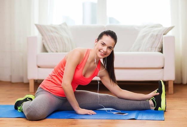 fitness, casa, tecnologia e concetto di dieta - adolescente sorridente che si allunga sul pavimento con smartphone e auricolari a casa