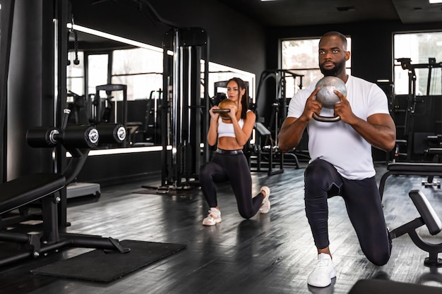 Fitness coppia uomo africano e donna caucasica in abbigliamento sportivo facendo esercizi di squat in palestra