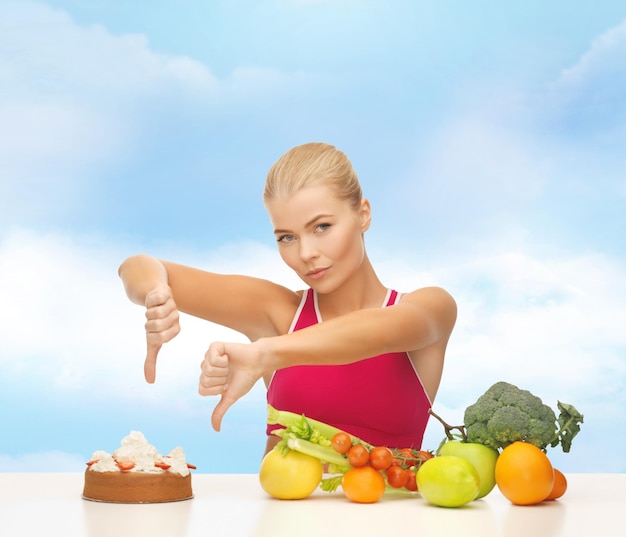 fitness, dieta, salute e concetto di cibo - donna sconvolta con cibo sano che mostra i pollici fino alla torta