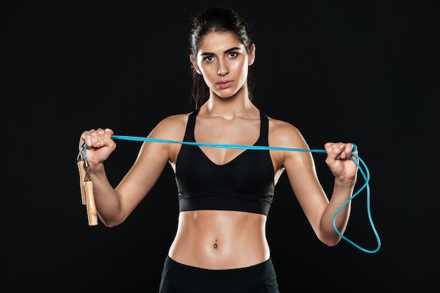 fitness donna in palestra in piedi sul muro nero e fare esercizi sportivi tenendo la corda per saltare