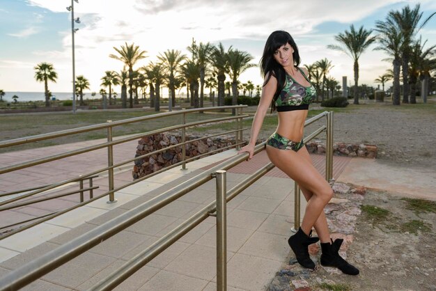 Fitness donna posa in abbigliamento sportivo con lunghi capelli neri nel parco cittadino al tramonto