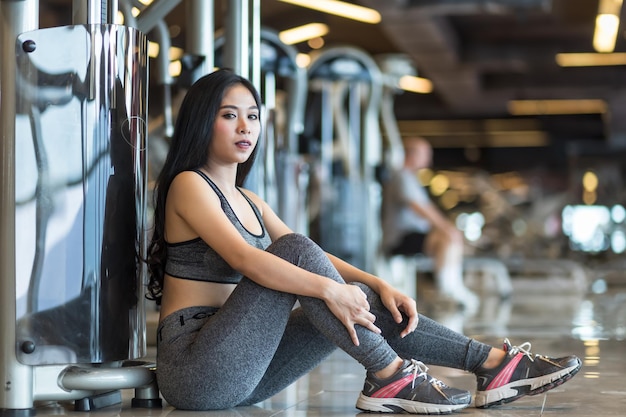 Fitness Donne asiatiche sedute all'interno di una palestra sportiva e un centro benessere fitness con attrezzature per esercizi sportivi Sfondo palestra