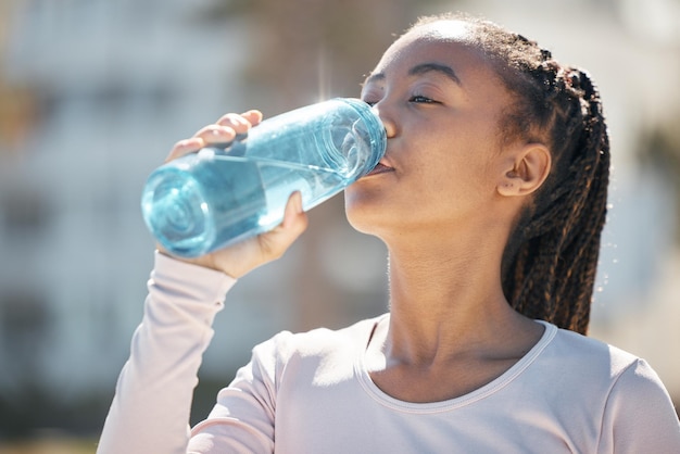 Fitness in acqua potabile e donna di colore in città urbana con sfida di allenamento per la salute, benessere e nutrizione Giovane atleta sportivo o corridore donna con bottiglia d'acqua per allenamento all'aperto