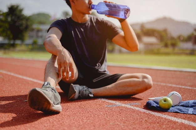 Fitness, jogging, corsa, esercizio fisico, stile di vita e concetto sano. Il giovane indossava tutte le parti del corpo e beveva acqua per prepararsi a fare jogging sulla pista di atletica intorno al campo di calcio.