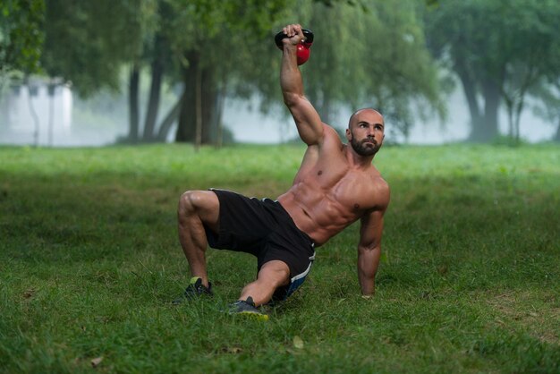 Fitness muscolare uomo equilibrio Kettlebells con una mano esercizio all'aperto