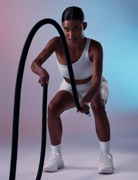 Fitness per ragazza e esercizio di allenamento con la corda per la pratica del muscolo cardio e della resistenza con sfondo da studio a colori Concentrati sulla salute e sul potere dell'allenamento della donna indiana con l'attrezzatura per l'allenamento del benessere in palestra