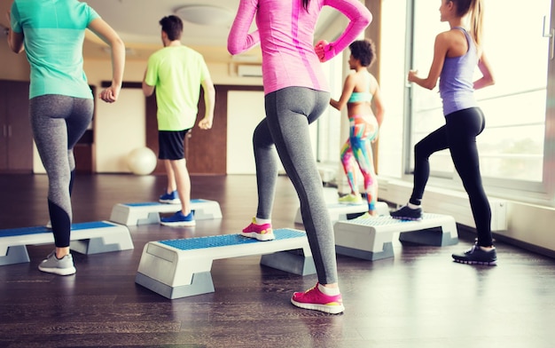 fitness, sport, allenamento, aerobica e concetto di persone - primo piano di persone che si allenano con gli stepper in palestra dal retro