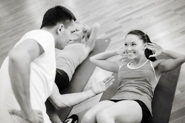 fitness, sport, allenamento, palestra e concetto di stile di vita - gruppo di donne sorridenti con allenatore maschio che fa sit up su stuoie in palestra