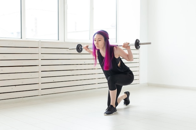 Fitness, sport, concetto di persone - la giovane donna in tuta sportiva è accovacciata con il bar.