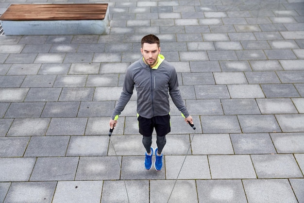 Fitness, sport, persone, esercizio e concetto di stile di vita - uomo che salta con la corda per saltare all'aperto