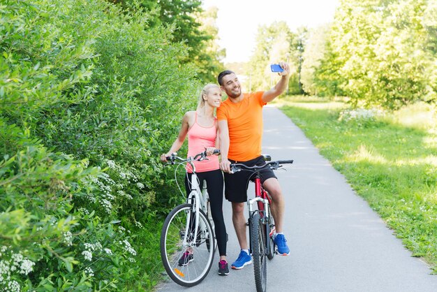 fitness, sport, persone, tecnologia e concetto di stile di vita sano - coppia felice con la bicicletta che si fa selfie con lo smartphone all'aperto