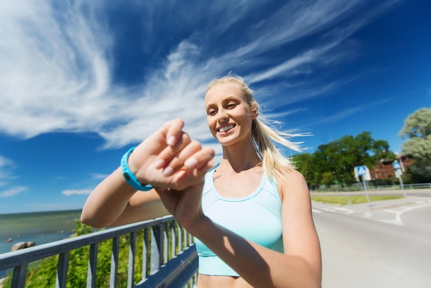 fitness, sport, persone, tecnologia e concetto di stile di vita sano - giovane donna sorridente con orologio per la frequenza cardiaca e auricolari che si esercitano all'aperto