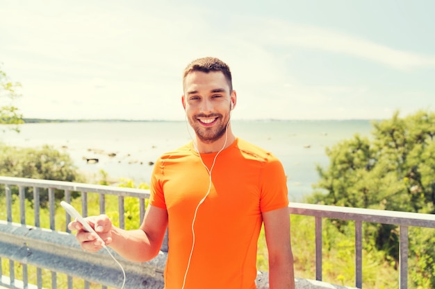 fitness, sport, persone, tecnologia e concetto di stile di vita sano - giovane sorridente con smartphone e auricolari che ascolta musica al mare estivo