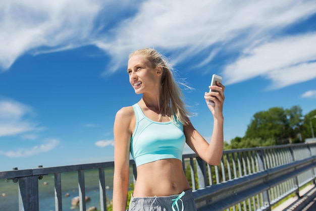 fitness, sport, persone, tecnologia e stile di vita sano concetto - giovane donna sorridente con smartphone che si esercita all'aperto