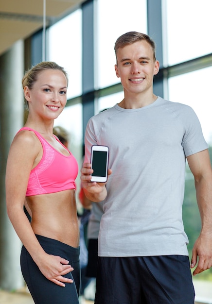fitness, sport, pubblicità, tecnologia e concetto di dieta - giovane donna sorridente e personal trainer con schermo vuoto dello smartphone in palestra
