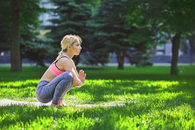 Fitness, yoga di addestramento della donna nella posa di squat regolare all'aperto nel parco, spazio della copia. La giovane ragazza esile fa esercizio. Stretching, benessere, calma, relax, concetto di stile di vita sano e attivo