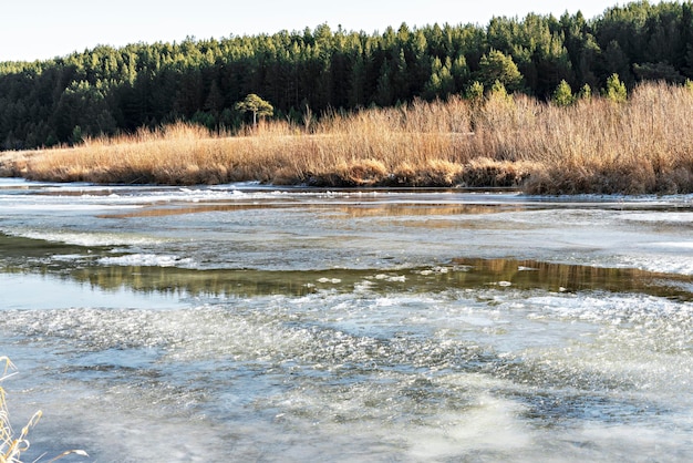 Fiume coperto dal primo ghiaccio e neve nel tardo autunno o all'inizio dell'inverno contro il paesaggio forestale