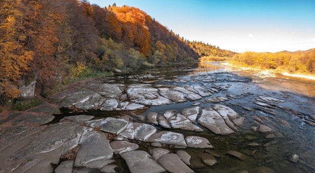 Fiume di montagna poco profondo ai piedi della collina con foreste di terracotta