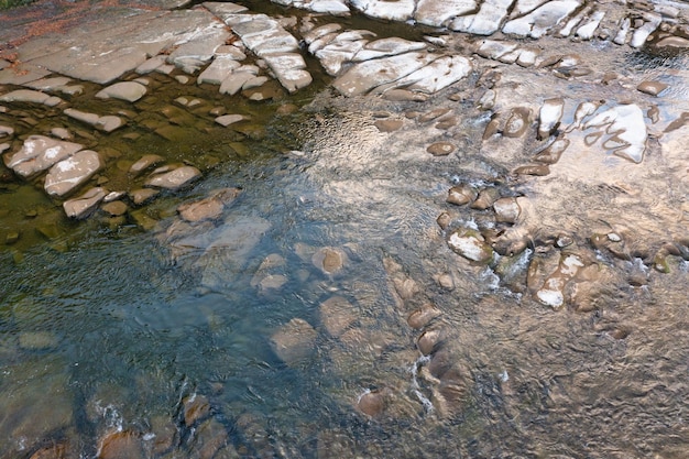 Fiume di montagna poco profondo con fondo roccioso e foreste di terracotta di conifere sui pendii delle colline sotto il cielo blu senza nuvole in una giornata autunnale