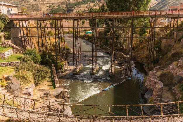 fiume vicino a costruzione in pietra e ponte di metallo a checacupe, cusco, perù