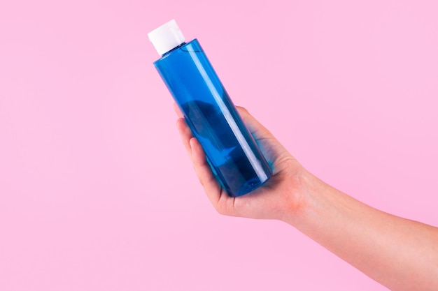 Flacone blu senza marchio per acqua micellare siero su sfondo rosa Tubo di plastica in mano femminile