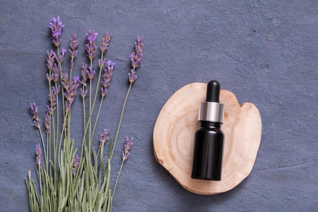 Flacone contagocce con prodotto cosmetico su podio in legno con fiori di lavanda su fondo in cemento vista dall'alto piatto