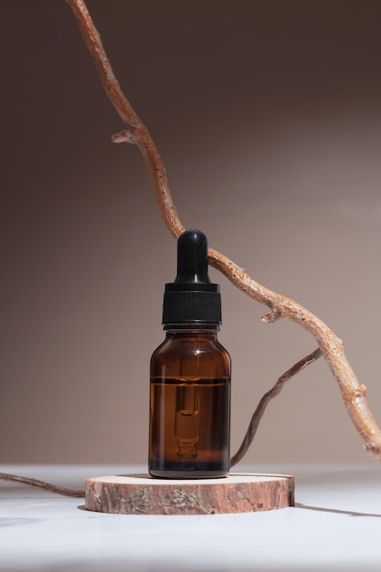 Flacone contagocce in vetro con supporto per olio essenziale o siero cosmetico su sfondo pastello con albero di ramo Prodotti omeopatici a base di erbe Cosmetici termali organici naturali