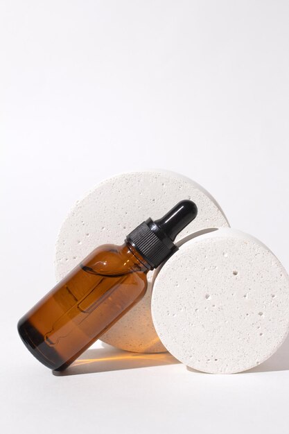 Flacone cosmetico con contagocce sul podio Contenitore per siero su sfondo bianco Concetto di prodotti di bellezza per cosmetici biologici