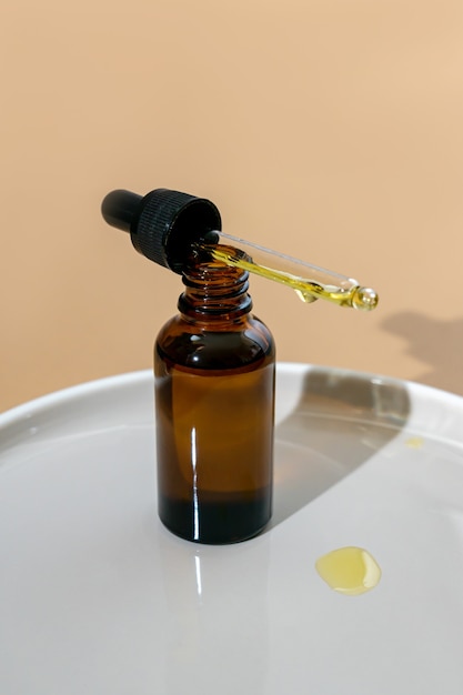 Flacone cosmetico in vetro scuro con contagocce su fondo cramico. Concetto di cosmetici naturali, olio essenziale naturale e prodotti per la cura della pelle.