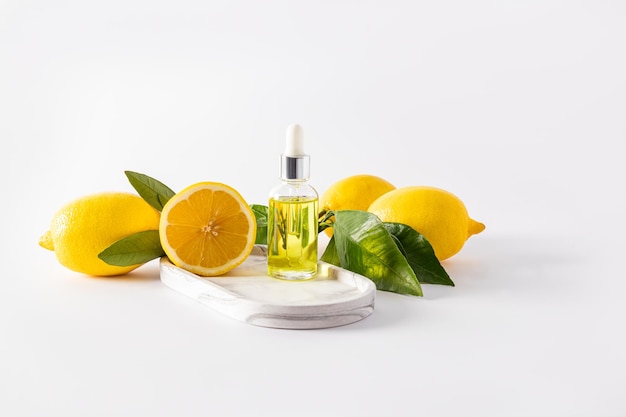 Flacone cosmetico trasparente con una pipetta con siero di limone per il viso si trova su un vassoio bianco con cosmetici naturali di frutti maturi