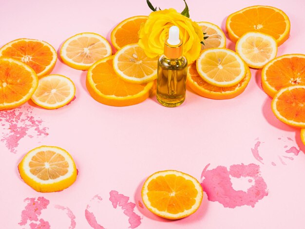 Flacone di siero di vitamina C con contagocce su sfondo rosa con fette di agrumi arancioni