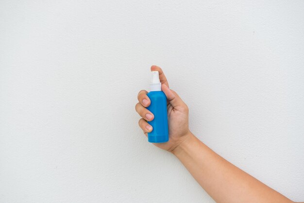 Flacone spray blu in mano su sfondo bianco