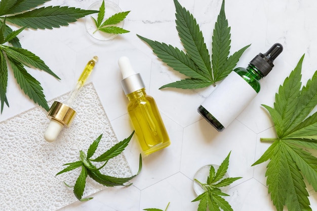 Flaconi contagocce cosmetici con etichetta vuota vicino a foglie di cannabis verde Mockup