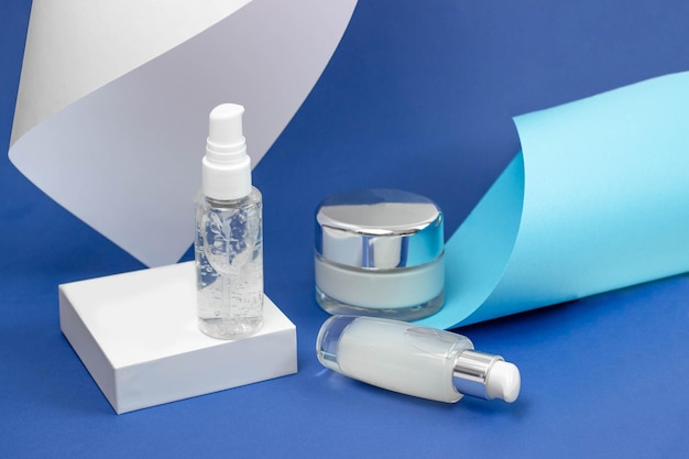 Flaconi cosmetici con siero, gel, crema viso su sfondo blu. Cosmetici per la pelle, minimalismo. Il concetto di procedure del salone.