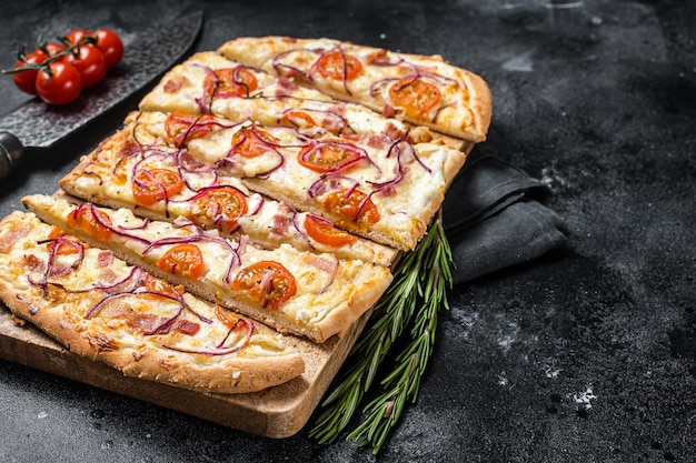 Flammkuchen fatto in casa o tarte flambee con crema di formaggio bacon pomodoro e cipolle Sfondo nero Vista dall'alto Spazio di copia