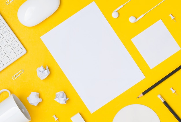 Flat lay di area di lavoro desktop con foglio di carta dello spazio vuoto su sfondo giallo