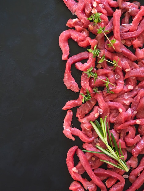 Flat-lay di carne fresca di manzo crudo sul tavolo nero. Sfondo di pezzi di vitello crudo. Manzo alla Stroganoff. Avvicinamento.