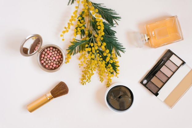 Flat lay fashion blogger Cosmetici e profumi decorativi e un ramo di fiori mimosa gialli su sfondo bianco