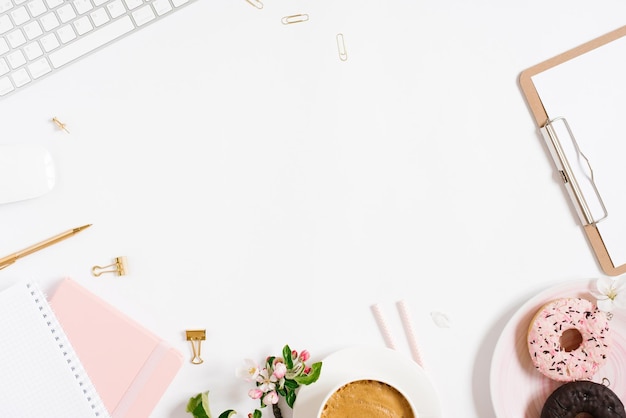 Flat lay home office area di lavoro femminile blogger sfondo bianco con tastiera moderna taccuino tazza di caffè ciambella e fiori di mela copia spazio su sfondo bianco