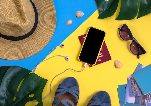Flatlay con foglie di monstera, smartphone, cuffie, cappello di paglia e altri accessori