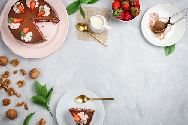 Flatlay con torta al cioccolato vegana, fragole, noci, cacao e altri ingredienti da dessert su sfondo di cemento con copyspace