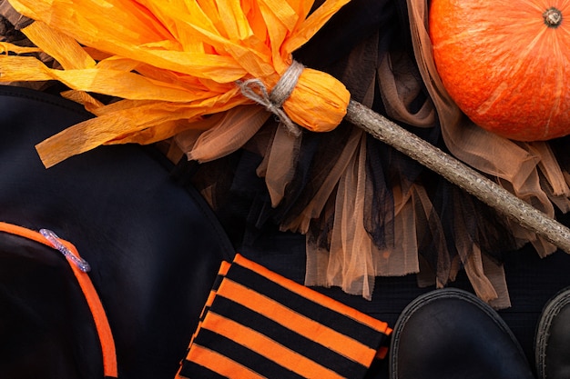 Flatlay di Halloween arancione e nero. Vestiti da strega: calze, stivali, cappello, scopa, gonna su sfondo nero