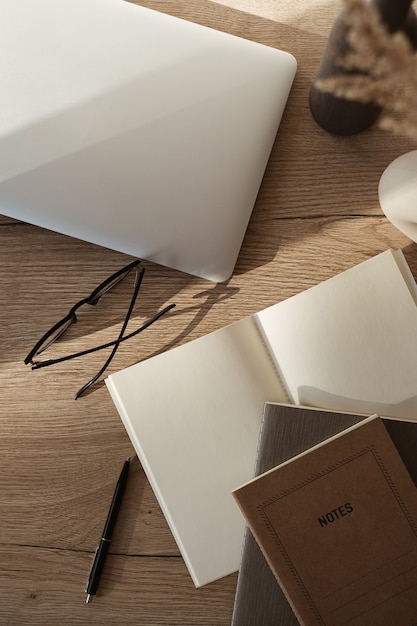 Flatlay di laptop, notebook, occhiali su sfondo di legno. Area di lavoro dell'ufficio domestico nelle ombre del sole