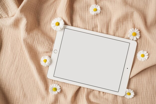 Flatlay di schermo vuoto tablet pad camomilla boccioli di fiori panno di lino beige neutro Estetica signora ragazza capo business lavoro blog modello con spazio mockup vista dall'alto laico piatto