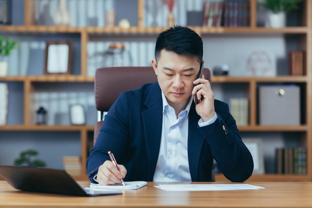 Flusso di lavoro Giovane uomo asiatico di successo bello che lavora in ufficio usando il telefono parlando al telefono Avvocato banchiere direttore seduto al tavolo che lavora con i documenti